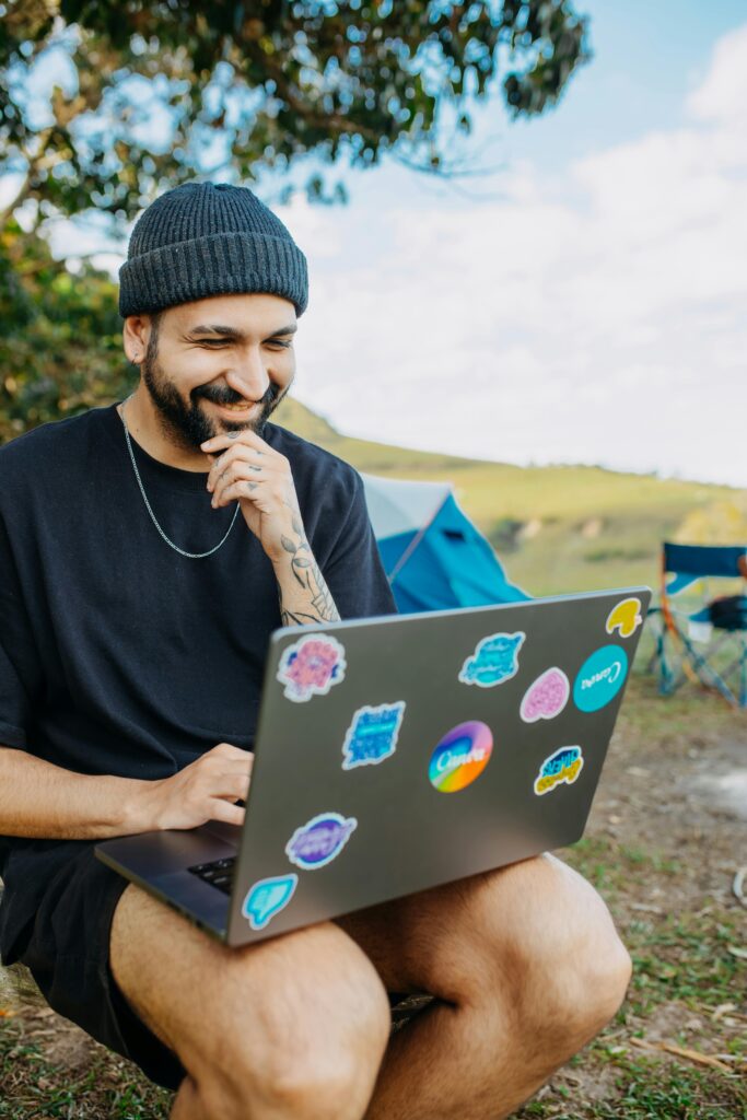 Smiling man using laptop with stickers while sitting outdoors in a meadow.