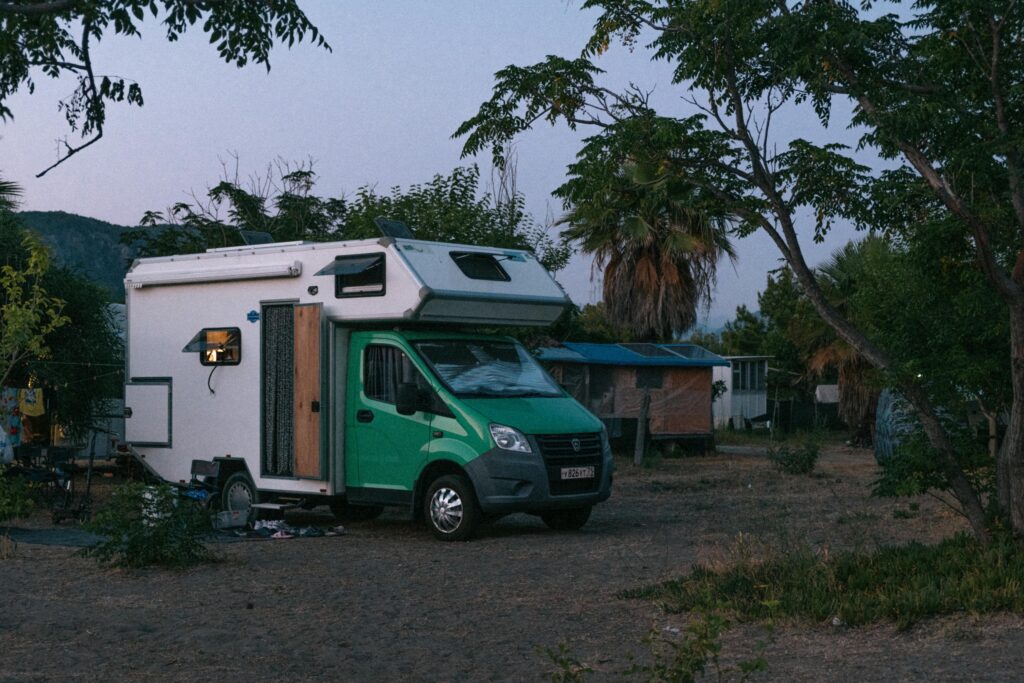 A serene camping van parked in a quiet forest setting at twilight, surrounded by lush trees and peaceful nature.